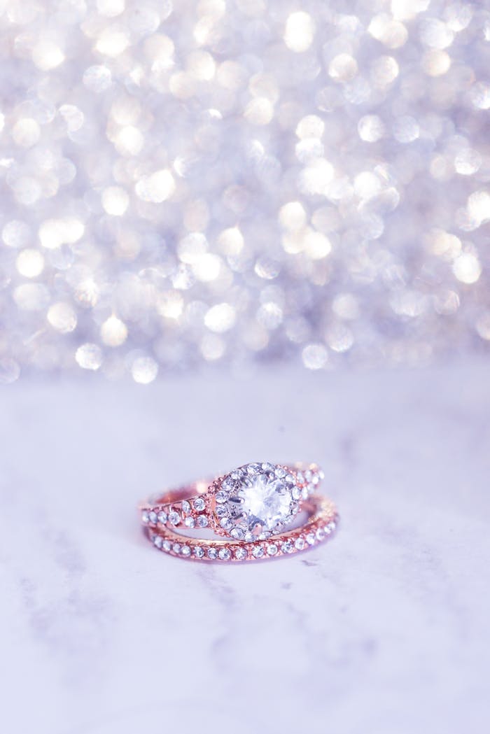 Close-up of a sparkling diamond engagement ring on a marble surface with bokeh background.